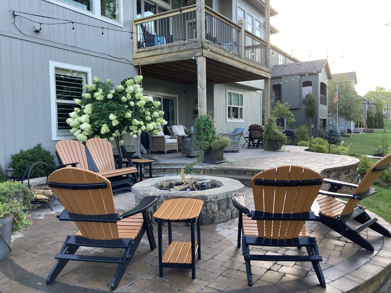 Paver patio with wooden Adirondack chairs around a fire pit under string lights