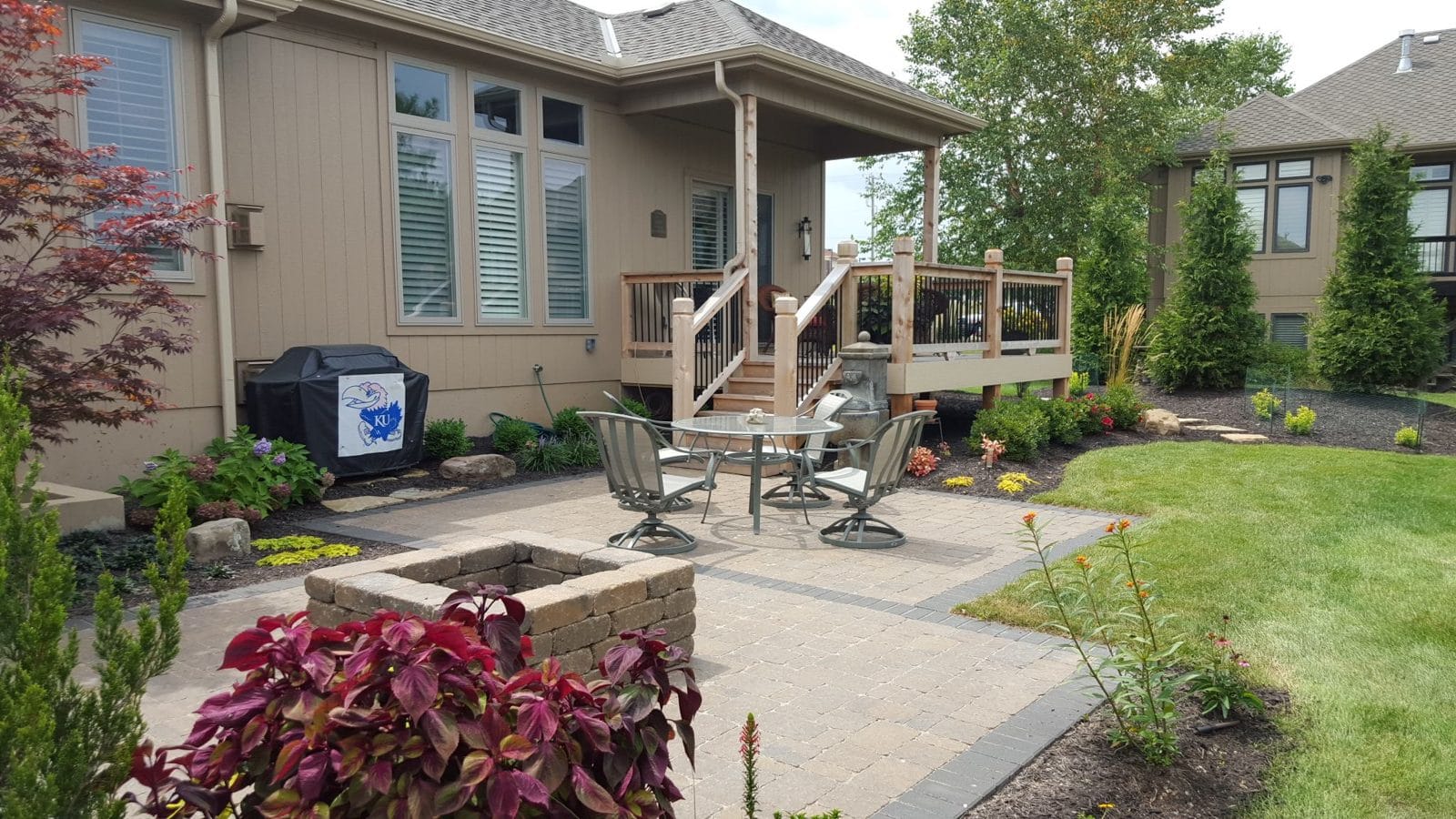 Paver patio with a gas fire pit, patio furniture, and colorful planting beds beside a home